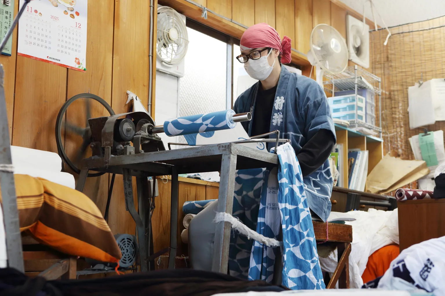 生地巻き機で手ぬぐいを巻く村井改（かい）さん。両手で適度に生地を引っぱりながら巻くことで、天日干しした手ぬぐいのシワを伸ばしていく。
