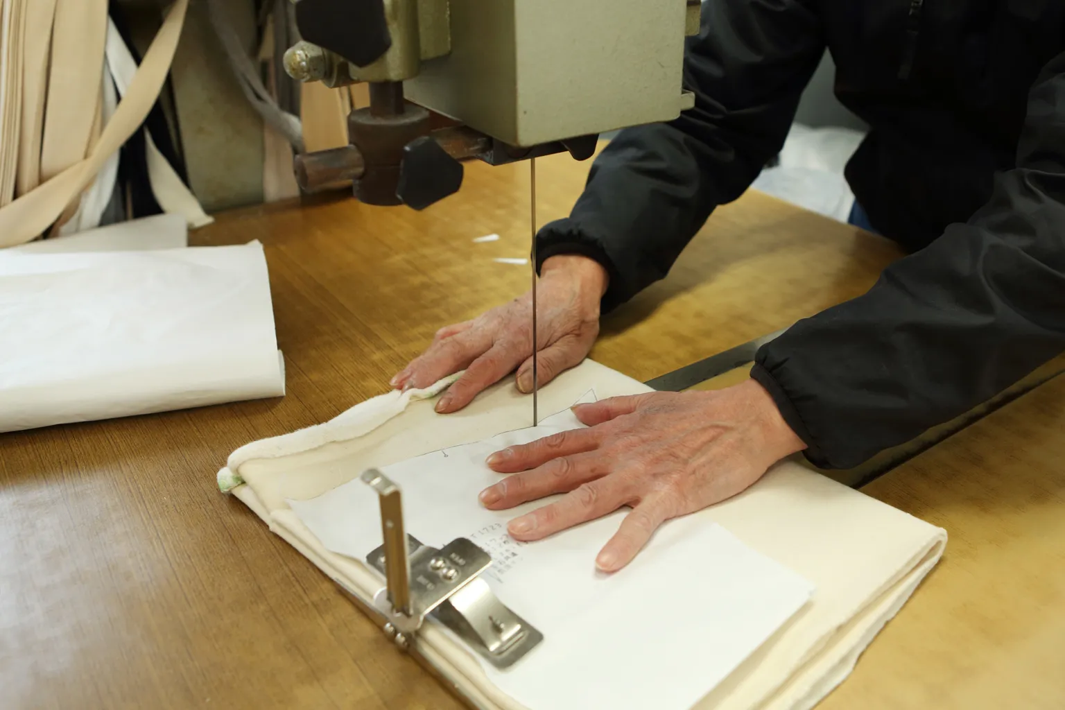 2階にある裁断場では、裁断職人が糸鋸のようなカッターを使って生地をパターンに合わせて切り出していく。筒状に織られた生地を重ね、無駄なく、ゆがみなく、正確に切り出すためには経験と技術が必要だ。