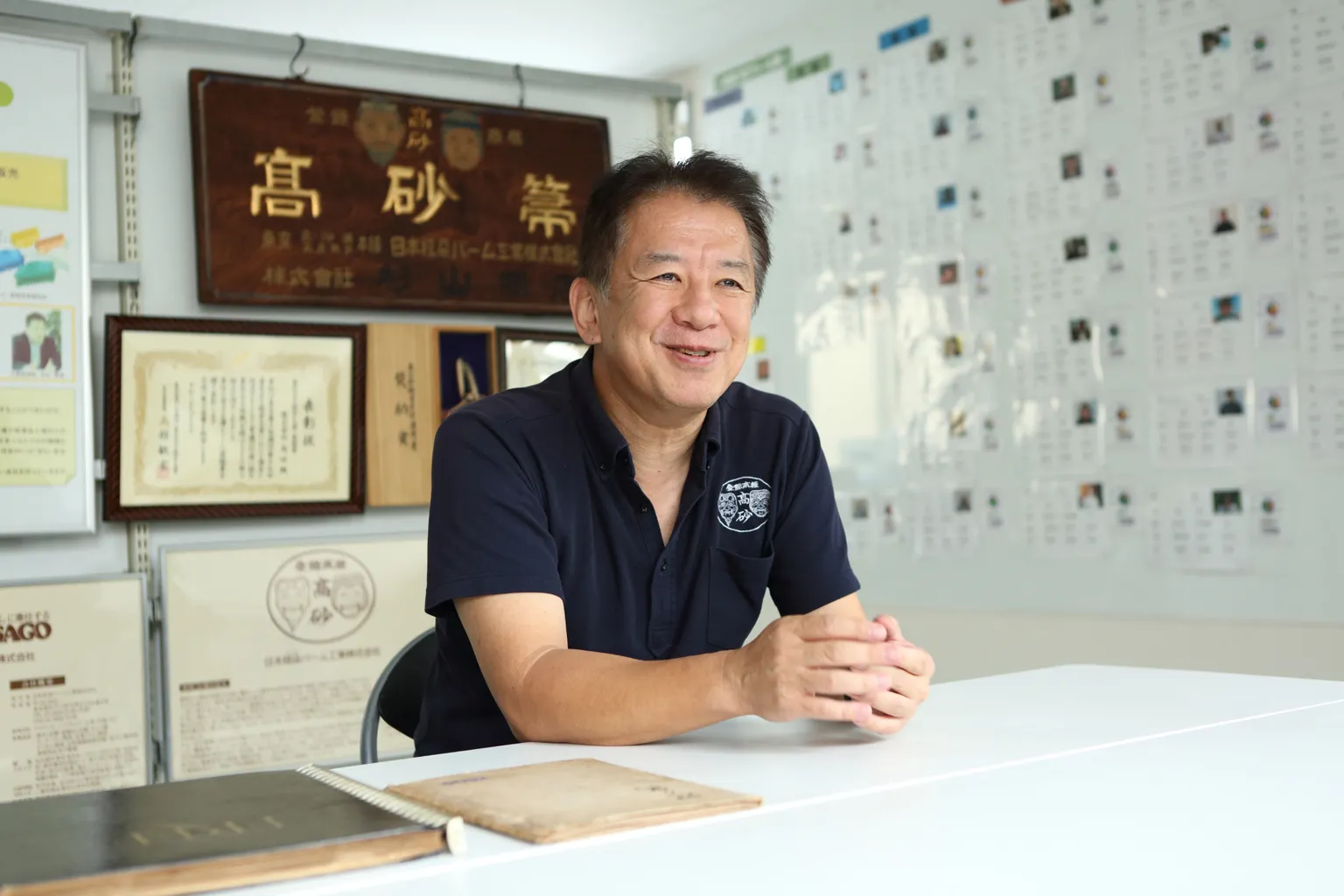 創業当時のいきさつを語る、株式会社高砂の4代目社長・吉田典靖さん。背後には社名の由来となった、自社製ほうきの商標「高砂箒」の歴史を感じさせる看板が。