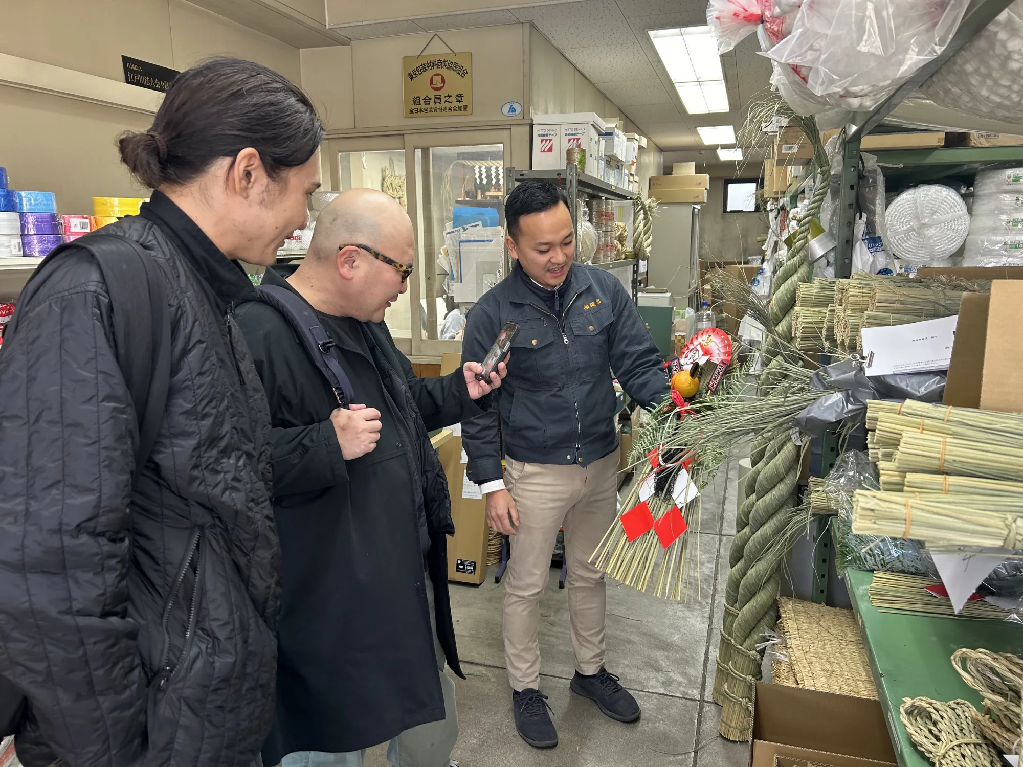 年末のしめ縄発送手配で多忙を極める縄忠の首代さん（右）。豪華なしめ縄を紹介してもらい、目を輝かせる柳さん（中）と中河さん（左）。