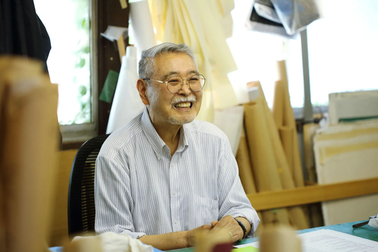 作業場で修業時代を振り返る笹谷さん。大きな作業机の周りには、表具の材料として使われるさまざまな種類の和紙や、大小のハケといった道具が並ぶ。