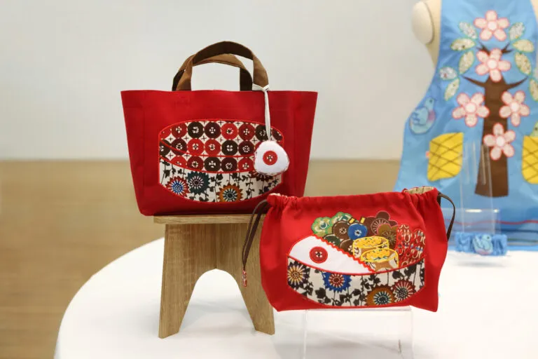 三橋工房の華やかな模様の生地を活かしたいと考え、お弁当の具材一つひとつをパッチワークにしてあしらった作品。このバッグ・巾着を使うことで、日常にささやかな彩りが生まれれば、という願いが込められています。