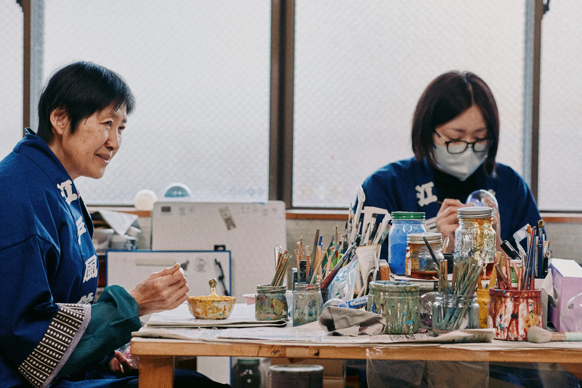 絵付けの作業場で、手を動かす惠美さん（左）・由香利さん（右）。テーブルの上にある無数の筆を色や用途に応じて使い分けながら、繊細な柄を描き出していく。